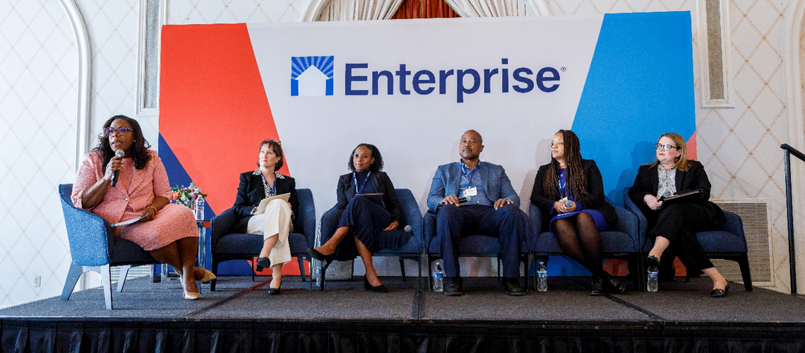 Panelists sitting in chairs on a platform, and a large poster behind them with the text 'Enterprise'.