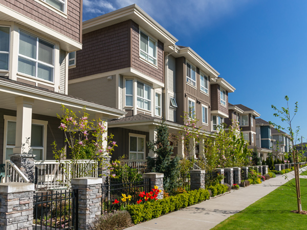 Photo of a row of three-story apartment buildings with trees and a sidewalk in front.