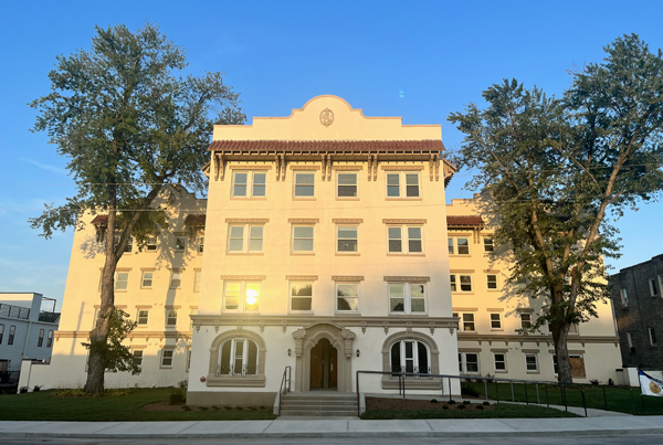 Four-story Spanish Colonial Revival residential building with a large tree on both sides. 