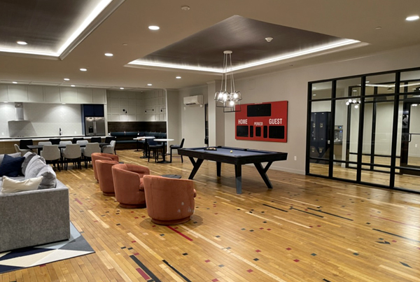 Resident community room with a sofa, chairs, a pool table, and kitchen and dining area. A red scoreboard is hanging on the wall.