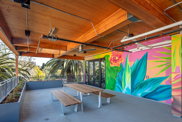 A covered terrace with a picnic table and benches next to a bright tropical mural.