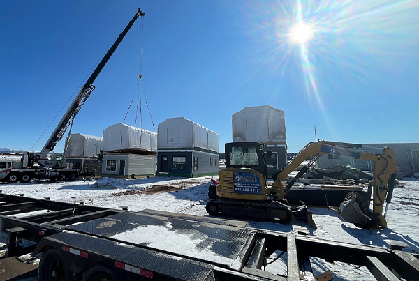 A crane installing a modular housing section at a rural neighborhood construction site.