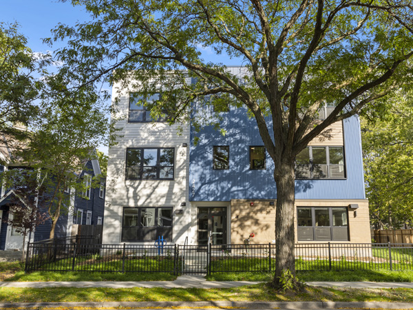 A modern three-story apartment building with a tree in the foreground.
