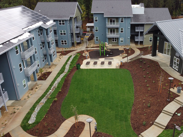 An interior courtyard with an open lawn and a patio surrounded by two 3-story buildings and a one-story building. 