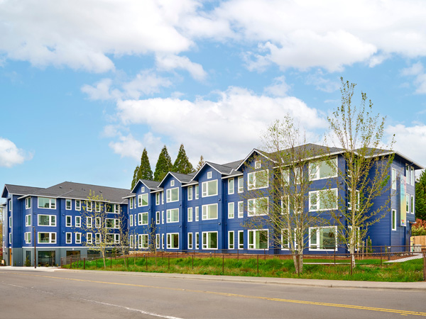 Exterior image of a three-story, L-shaped apartment building painted bright blue with white trim. 