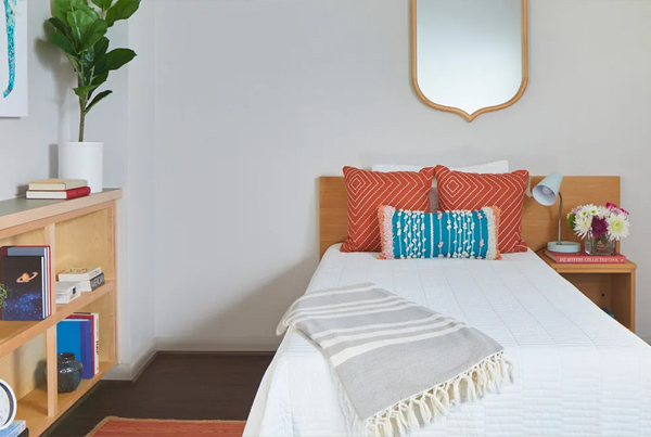 A made bed with a lamp and flower pot on the nightstand. 