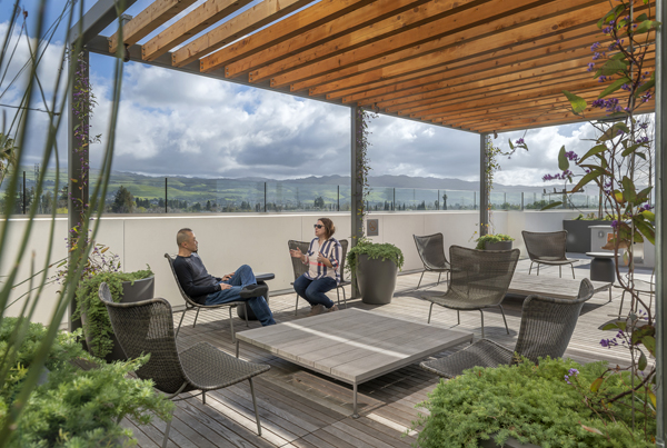 Two people talking under a pergola on a furnished outdoor patio.