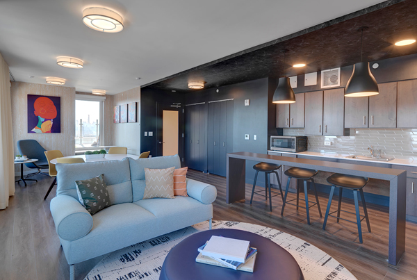 Interior communal space with a kitchenette and bar seating, a loveseat and coffee table in the foreground, and a table with chairs in the background.