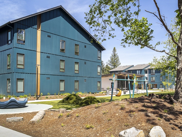 Two 3-story residential buildings with a playground in the foreground and a landscaped walking path alongside it.  