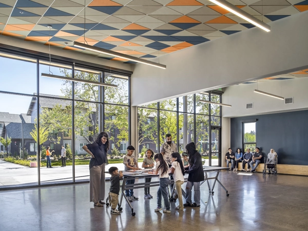 Children gathered around a table in a large, open room with floor-to-ceiling windows. 