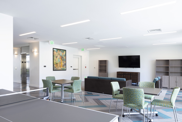 Community room with a pingpong table, chairs around two tables, and a sofa facing a television.