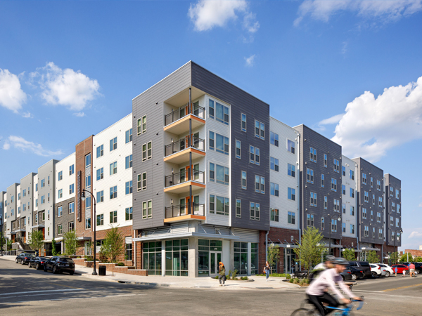 The front and side façades of a four-story apartment building, constructed over ground-floor retail. 