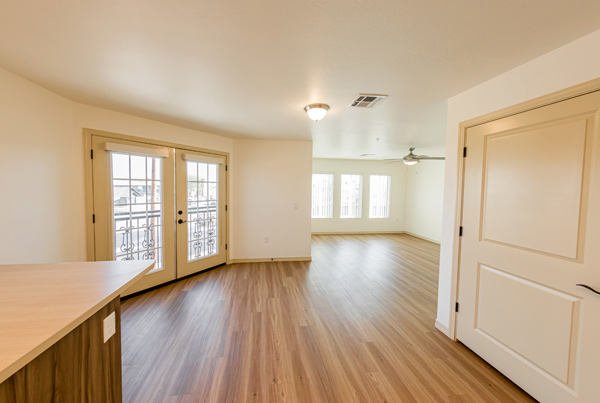 An apartments’ unfurnished living and dining area framed by double doors leading to a balcony. 