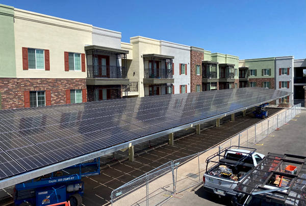 A parking lot covered by solar panels with a three-story building in the background and two utility trucks in the foreground. A parking lot covered by solar panels with a three-story building in the background and two utility trucks in the foreground.