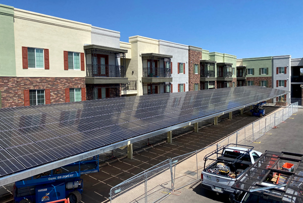 A parking lot covered by solar panels with a three-story building in the background and two utility trucks in the foreground.