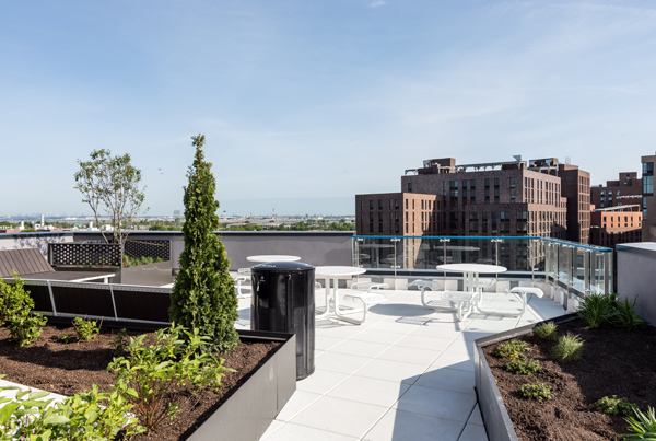 A landscaped apartment building rooftop with tables and benches.