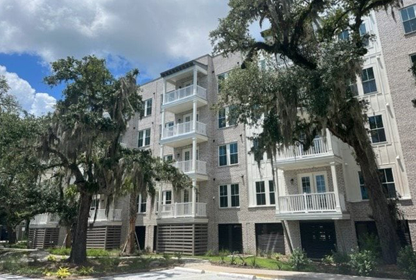 Side of small apartment building with four floors of units, some of which have balconies.