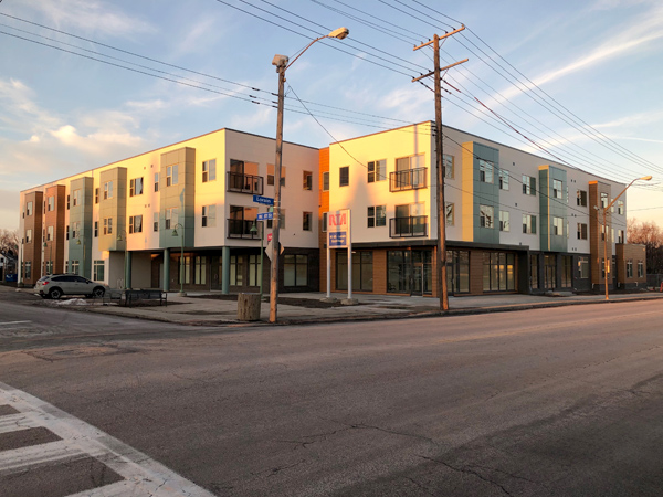 Photograph of a three-story apartment building, taken from a 90 degree angle across an intersection.  