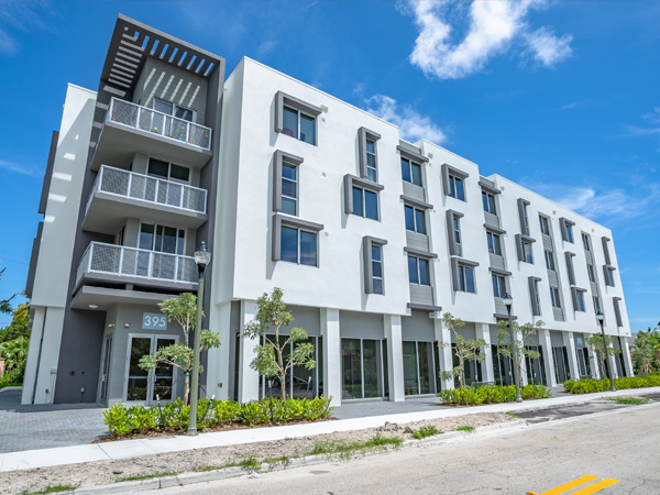 Perspective photo of a four-story building’s frontage revealing stacked balconies on the left corner of the building.