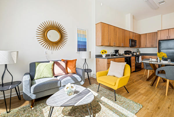 A sunny living room, kitchen, and dining area in a modern, furnished apartment.