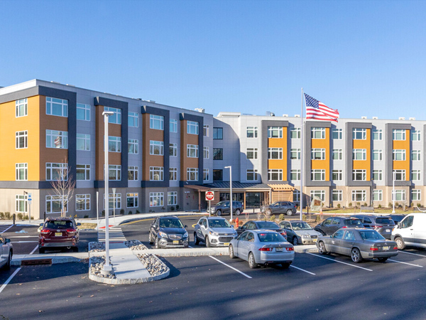 Photograph of a four-story residential building with a parking lot in front.