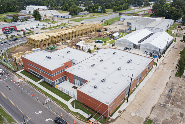 Aerial view of factory and warehouse converted into apartments, with an adjacent apartment building under construction.