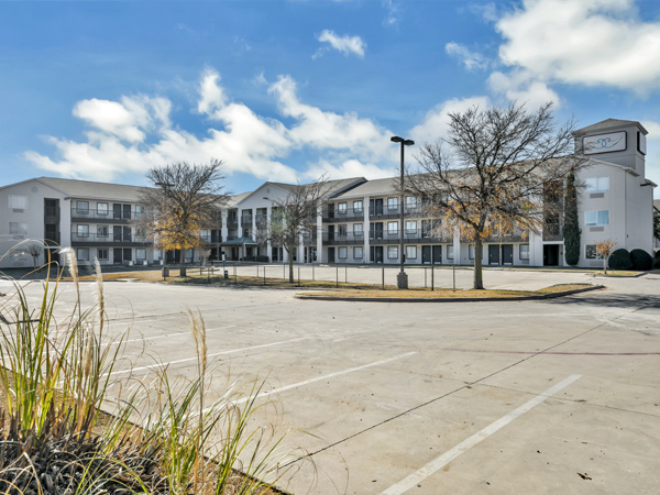  Photo of a three-story apartment building with a parking lot in the forefront.