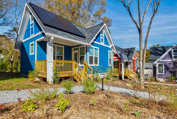 Three small adjoining homes with plants and vegetation in front.