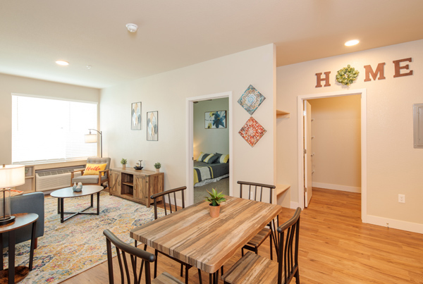 A dining and living room in an apartment with an open door to a bedroom in the back.