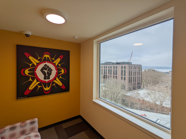 Photo of the corner of a room with a large window to the right and Native artwork to the left. 