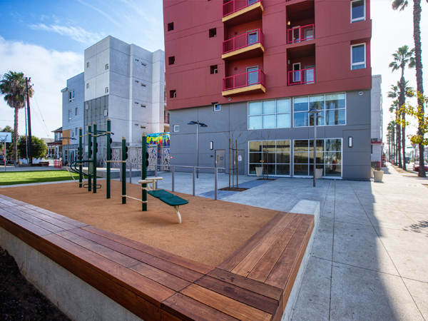 Photograph of a miniature playground and open lawn that are in front of a multi-colored building.  