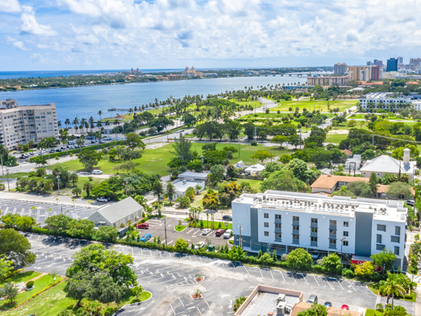 Aerial photo with parking lots and a mid-rise building in the foreground and a greenspace, water body and city skyline in the background. 