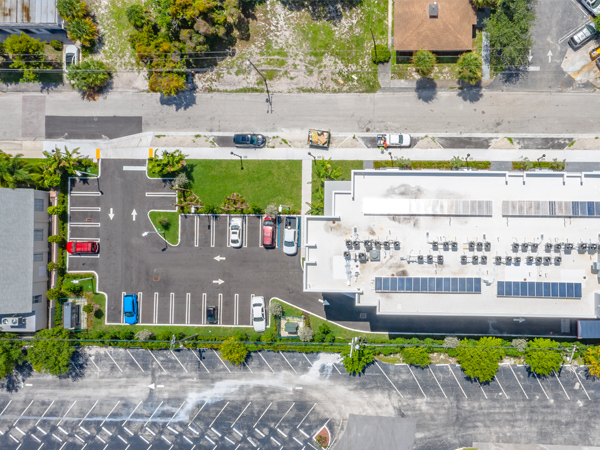 Aerial view of corner parcel that contains a parking lot between two buildings and greenery on the property edges.  