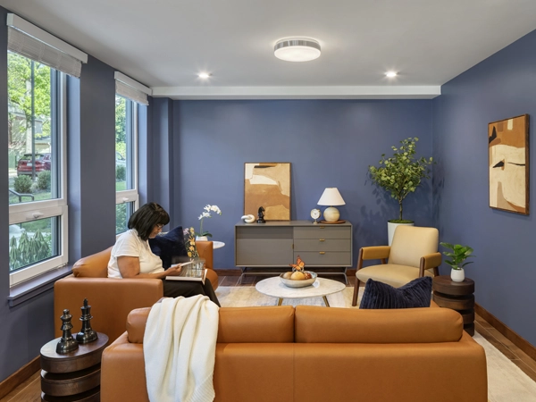 A woman reading in a room with two orange couches and blue walls.