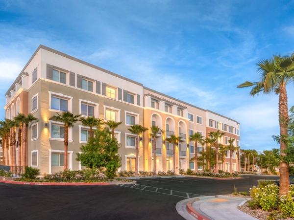 A four-story building with a stucco exterior in a desert environment, lined with palm trees.