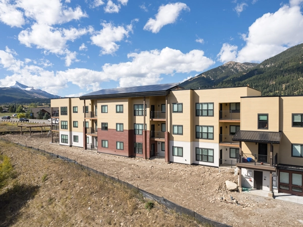 Exterior photograph of three-story apartment building with mountains in the background.