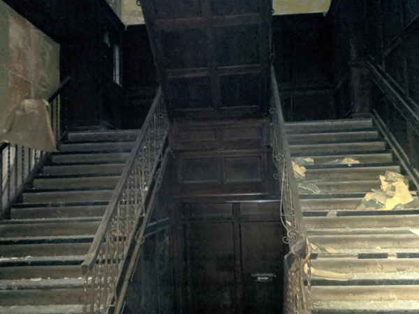 A dilapidated interior wooden staircase shows the building’s damaged state before its renovation.