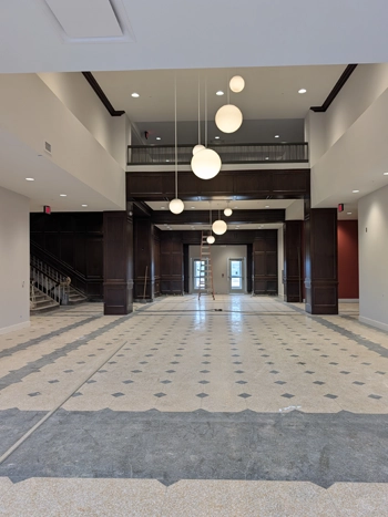 A restored lobby with dark woodwork, high ceilings, historic tile floors, and modern lighting.