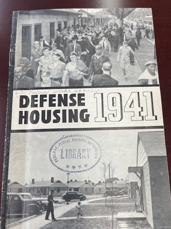 The front cover of a brochure on a desk, titled "Defense Housing: 1941".
