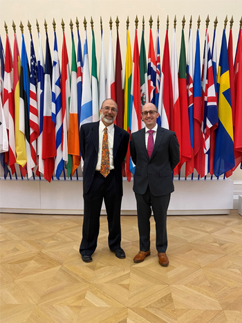 Kurt Usowski (left) and Aaron Weaver (right) stand in front of a wall of different country flags.