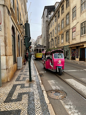 Image of a passenger scooter and tram on a European city.