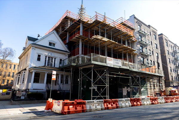 A residential luxury building under construction next to an old house in New York City.