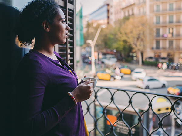  Photo of a woman holding a cup while standing on a balcony.