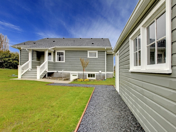  A grey house on a green lawn and a matching detached garage.