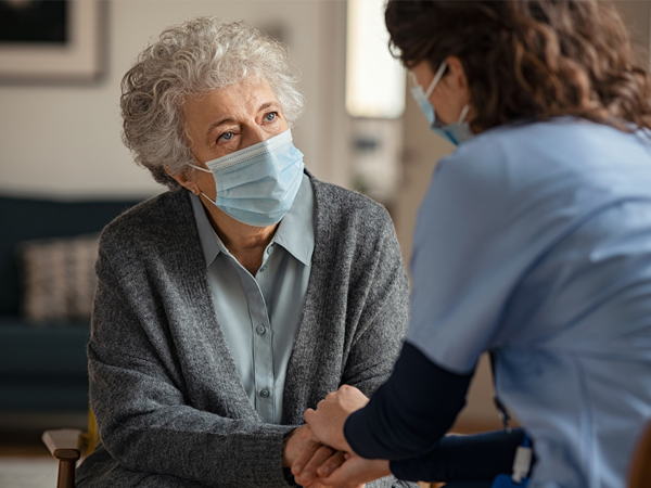Photo of an elderly woman holding hands with a doctor, both wearing masks.