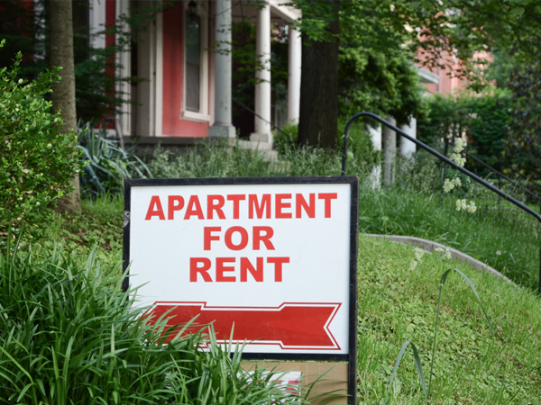 Photo of an apartment building with a sign in the foreground saying “APARTMENT FOR RENT.”