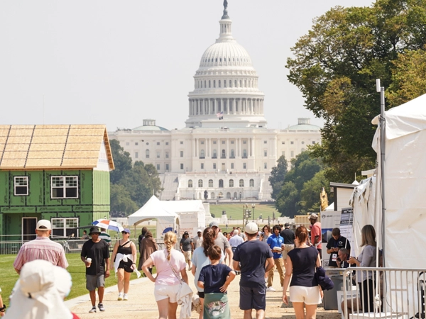 A crowd of people at the National Mall in Washington, D.C., with exhibits lined up on the right and a model house on the left. The United States Capitol can be seen in the background.