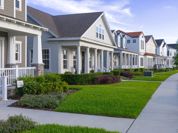 A row of houses with green lawns and shrubbery, and a sidewalk in front of them.