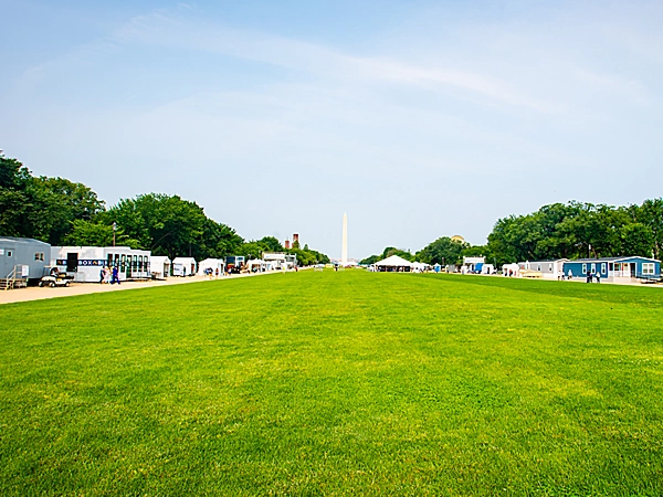 A grassy lawn at the National Mall, with exhibit houses on both sides of the lawn and the Washington Monument in the distance.