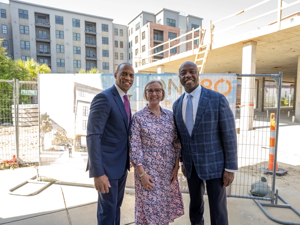 Scott Turner (left) poses with a woman and man in front of a sign that reads "One80 Place" amidst development.